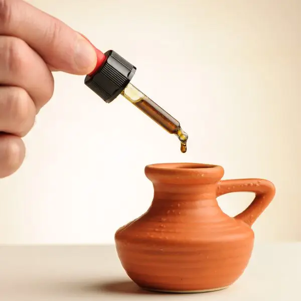 Pipette mit einem Tropfen CBD-Öl 14,75%, der in ein kleines Terrakotta-Krüglein fällt