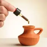 Pipette mit einem Tropfen CBD-Öl 16,73%, der in ein kleines Terrakotta-Krüglein fällt