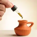 Pipette mit einem Tropfen CBD-Öl 5,65%, der in ein kleines Terrakotta-Krüglein fällt