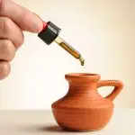 Pipette mit einem Tropfen CBD-Öl 8,77%, der in ein kleines Terrakotta-Krüglein fällt