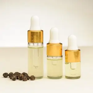 Drei Fläschchen mit schwarzem Pfeffer ätherischem Öl (2 ml, 3 ml und 4 ml) neben schwarzen Pfefferkörnern